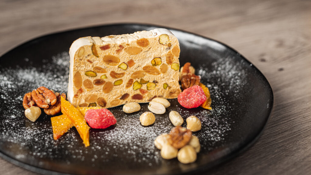 Vers gemaakte ambachtelijke nougat van ZinZetion met groene pistachenoten en rode gedroogde aardbeien, geserveerd bij een kop thee op een houten plank.